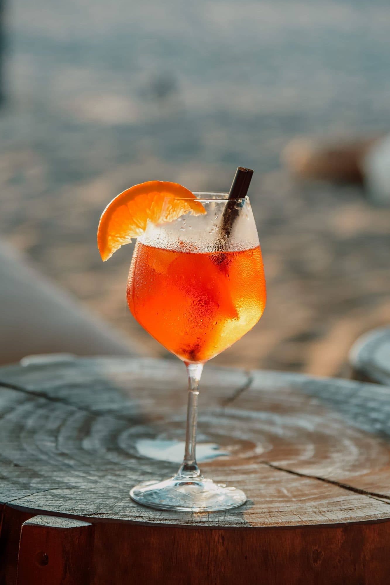 An orange spritz on a wooden table by the beach