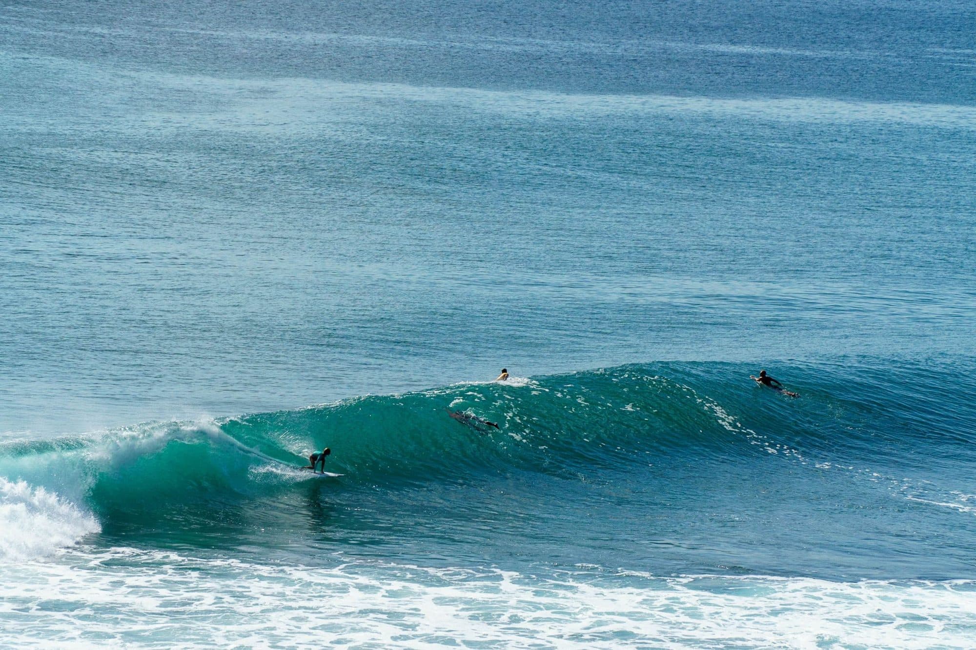 Three surfers riding waves off a Bali beach
