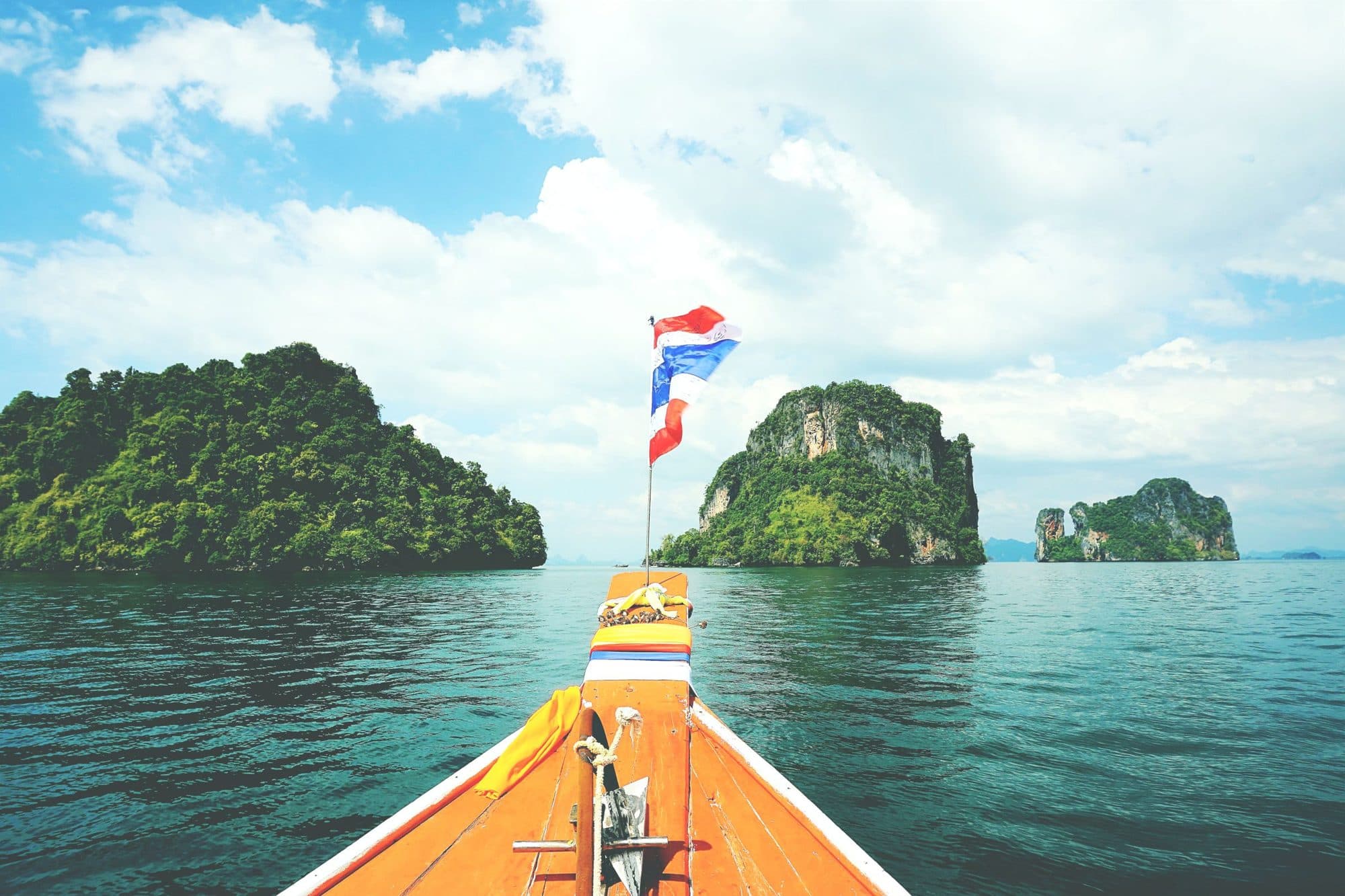 The bow of a long-tail boat heading toward limestone islands