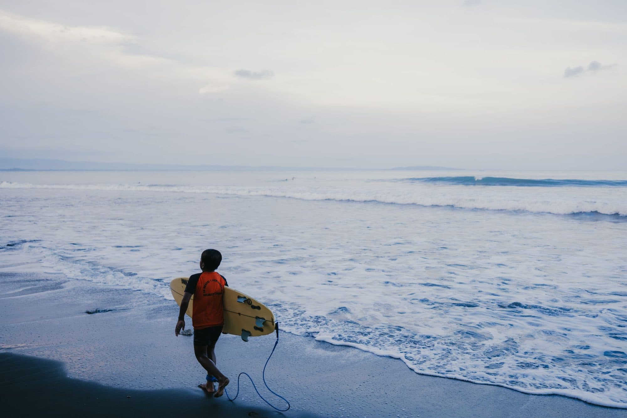 A surfer walking into the water with a board