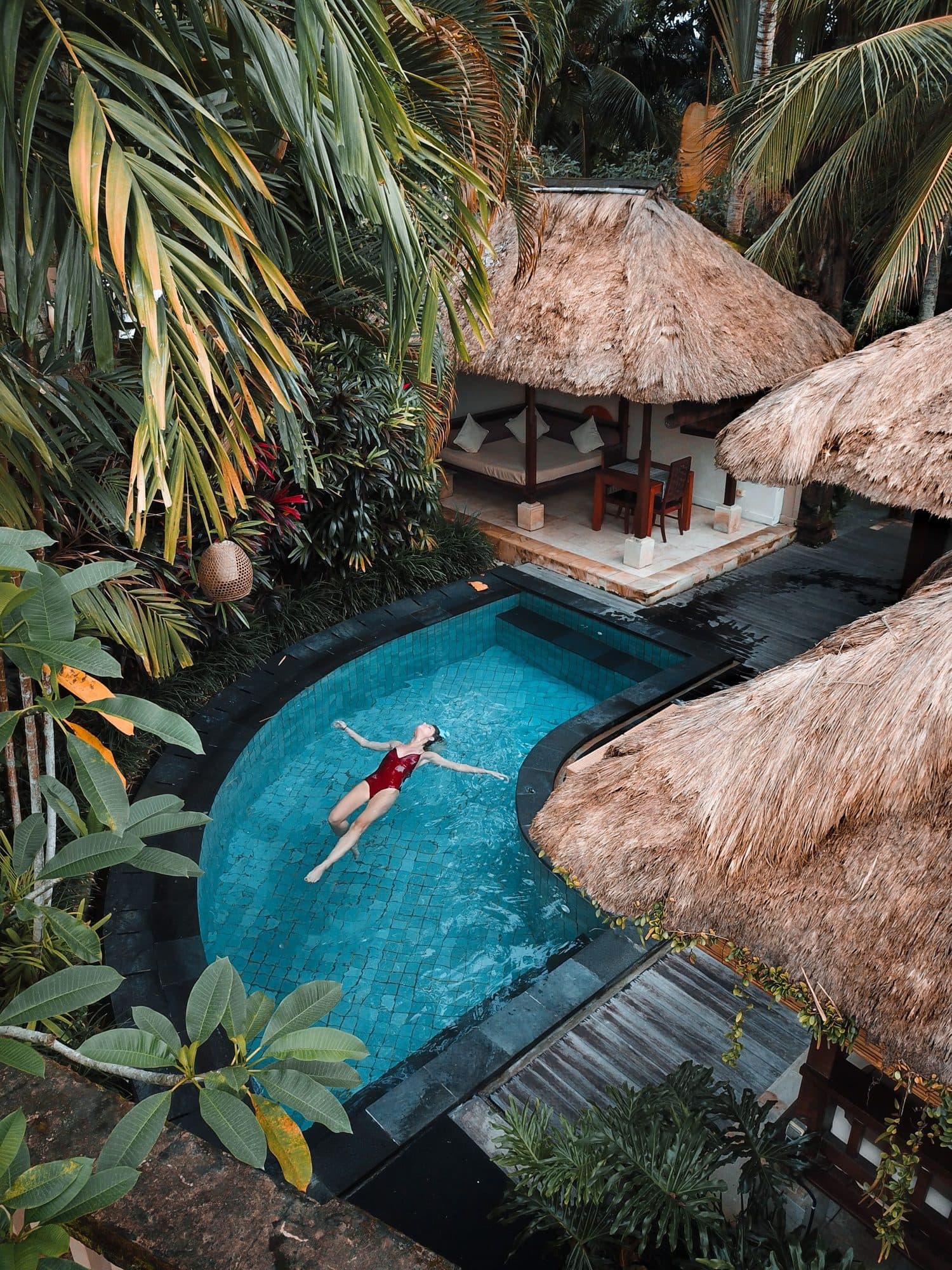 A swimmer floating in a curved pool beneath thatched roofs