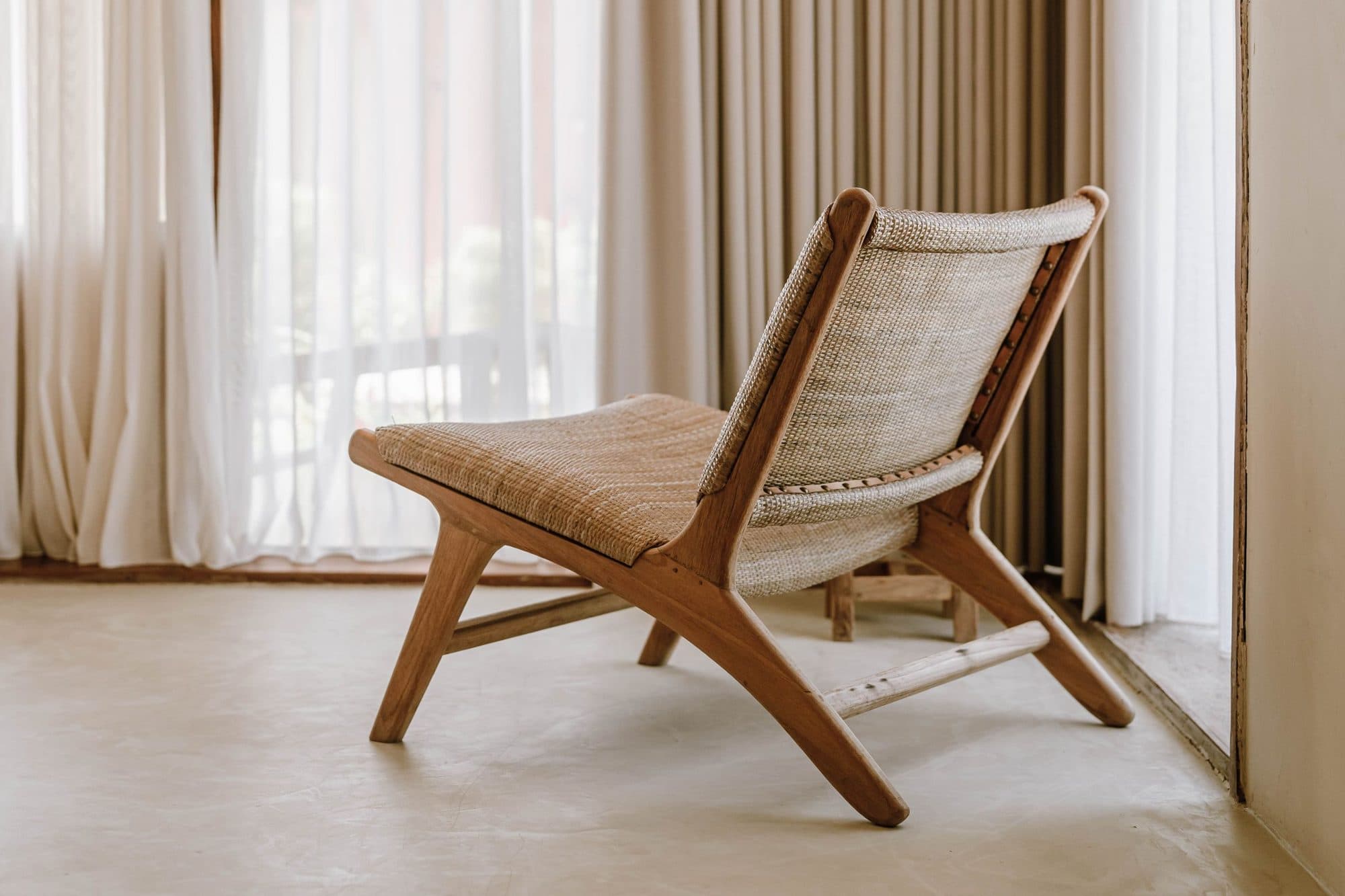 A woven lounge chair beside a sheer curtain in a boutique hotel room