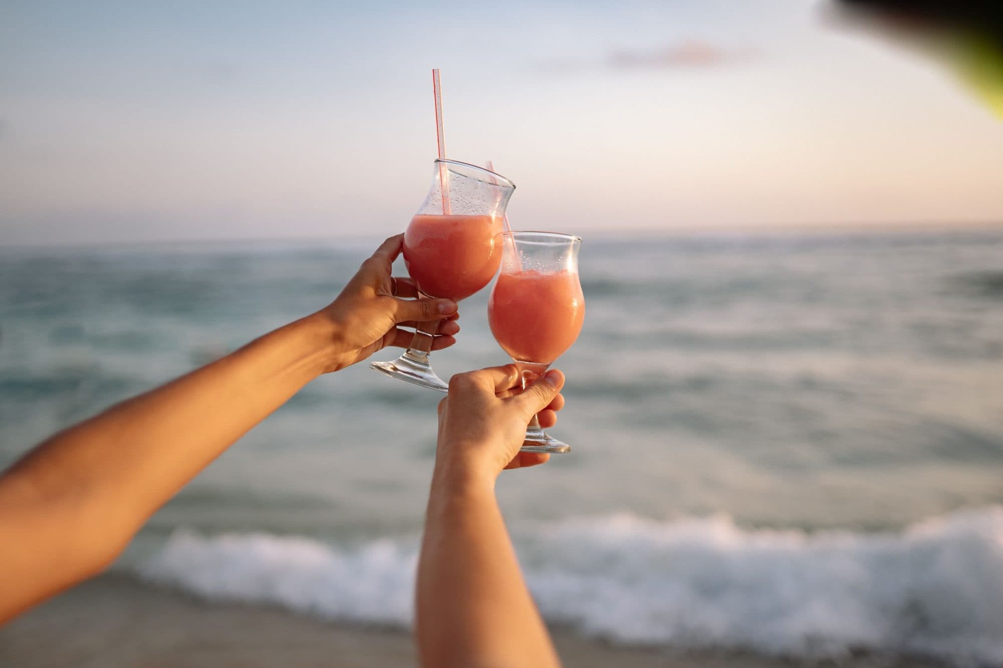 Two hands raising cocktails over the sea