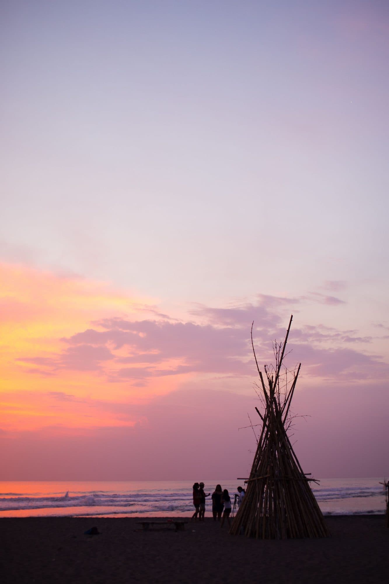 Bamboo tipi silhouetted against a pink sunset on Batu Bolong beach