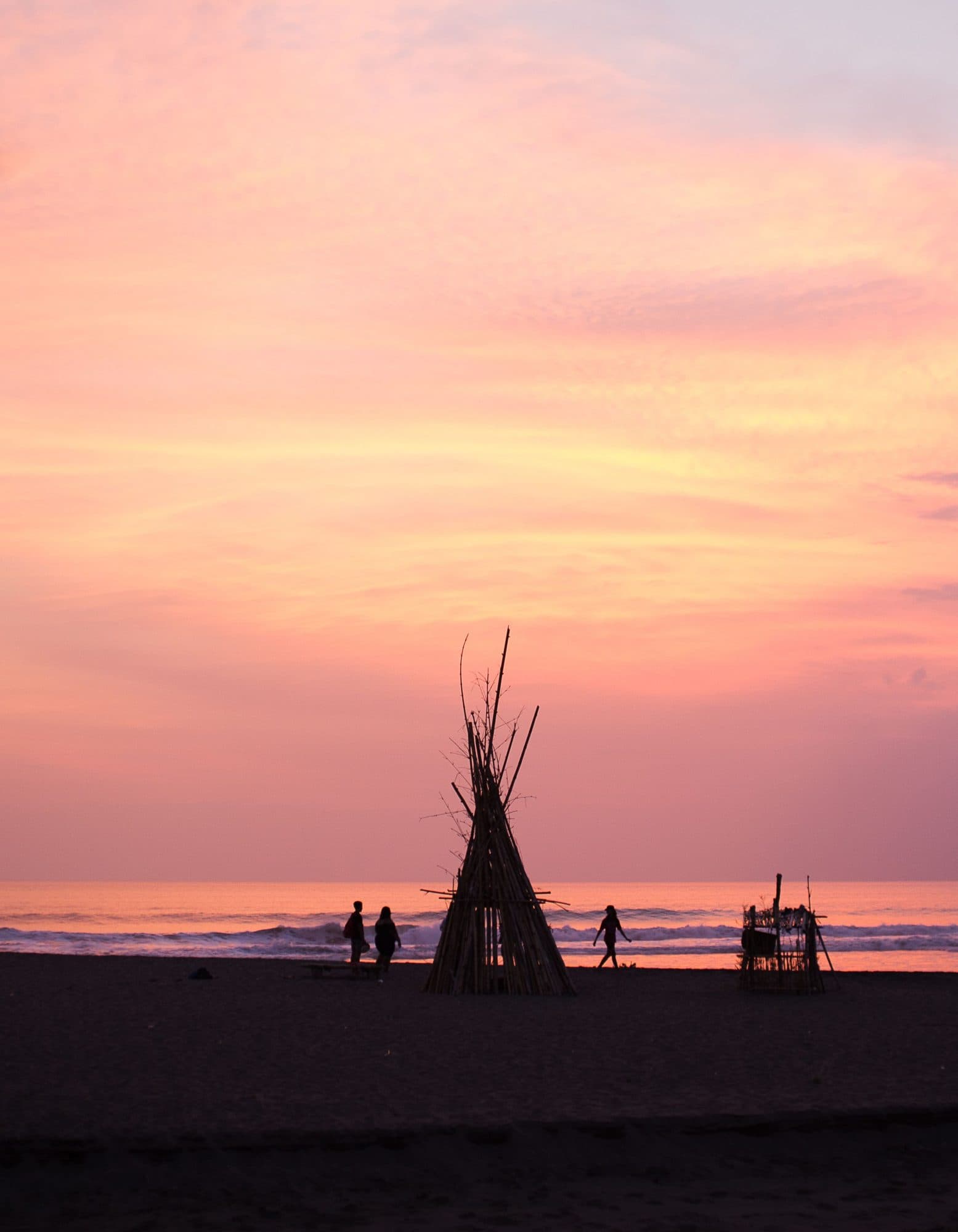 A tipi silhouetted on the sand under a pink sky