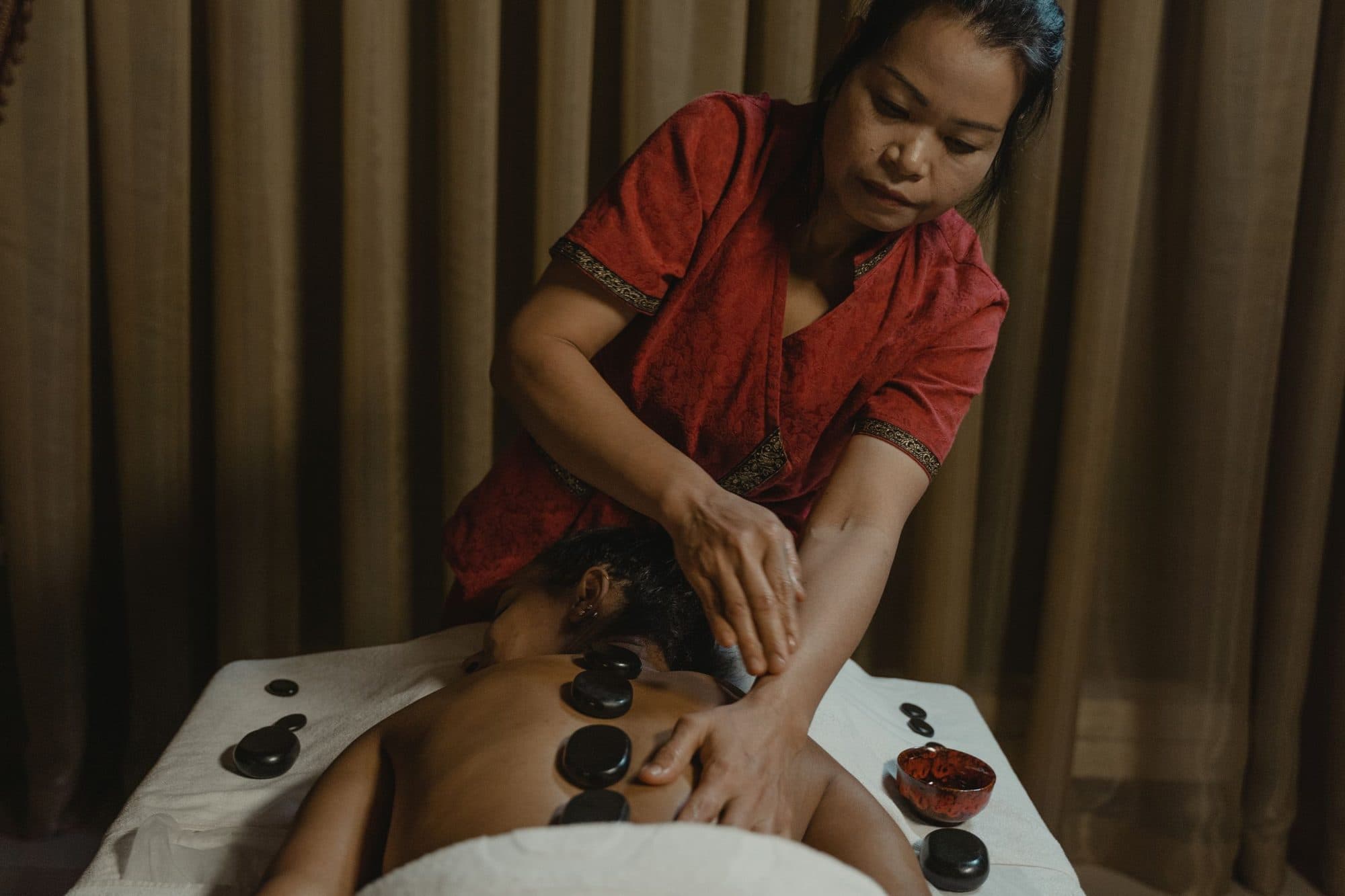 A therapist giving a hot stone massage in a calm indoor spa room