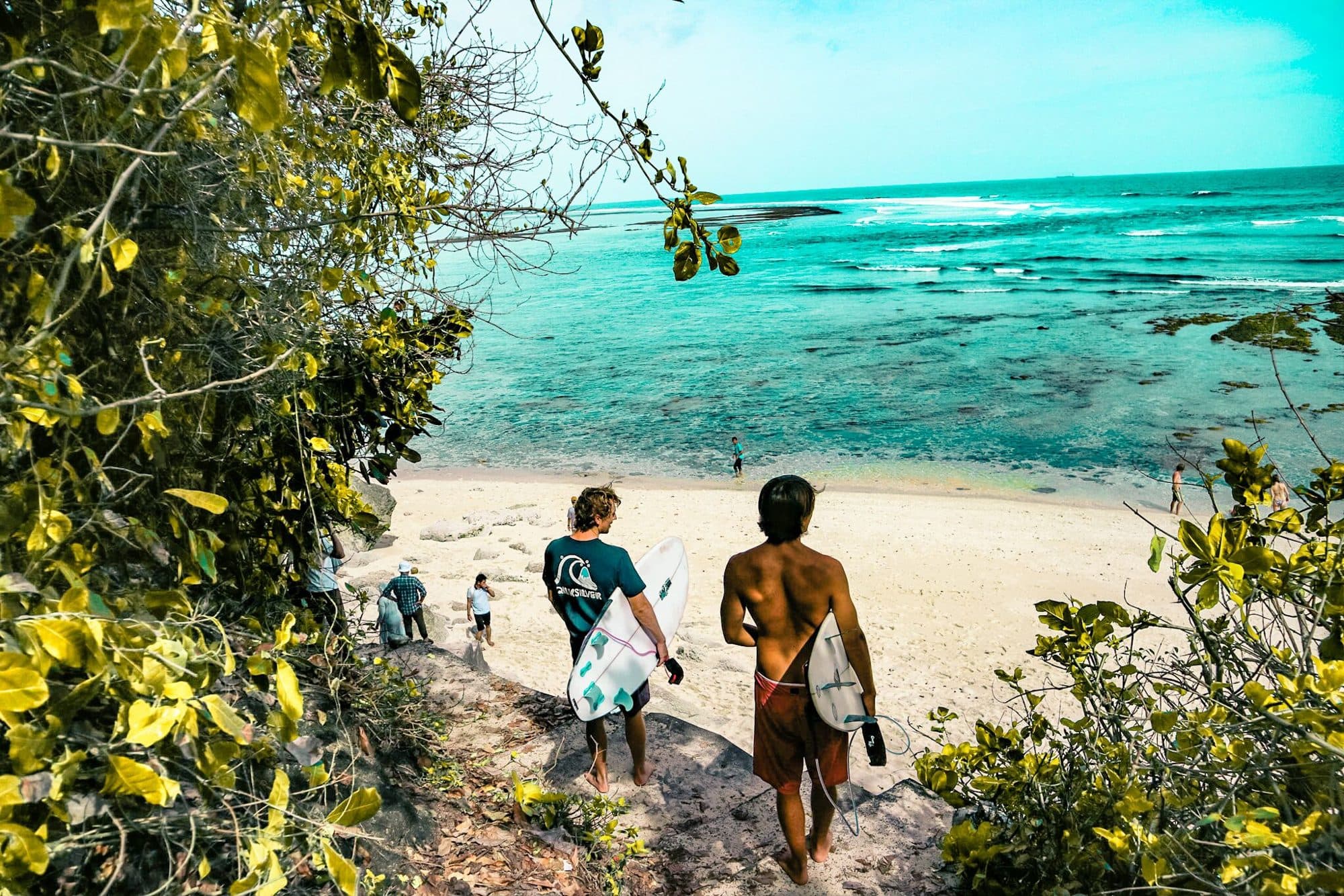 Two surfers carrying boards through the jungle onto a beach