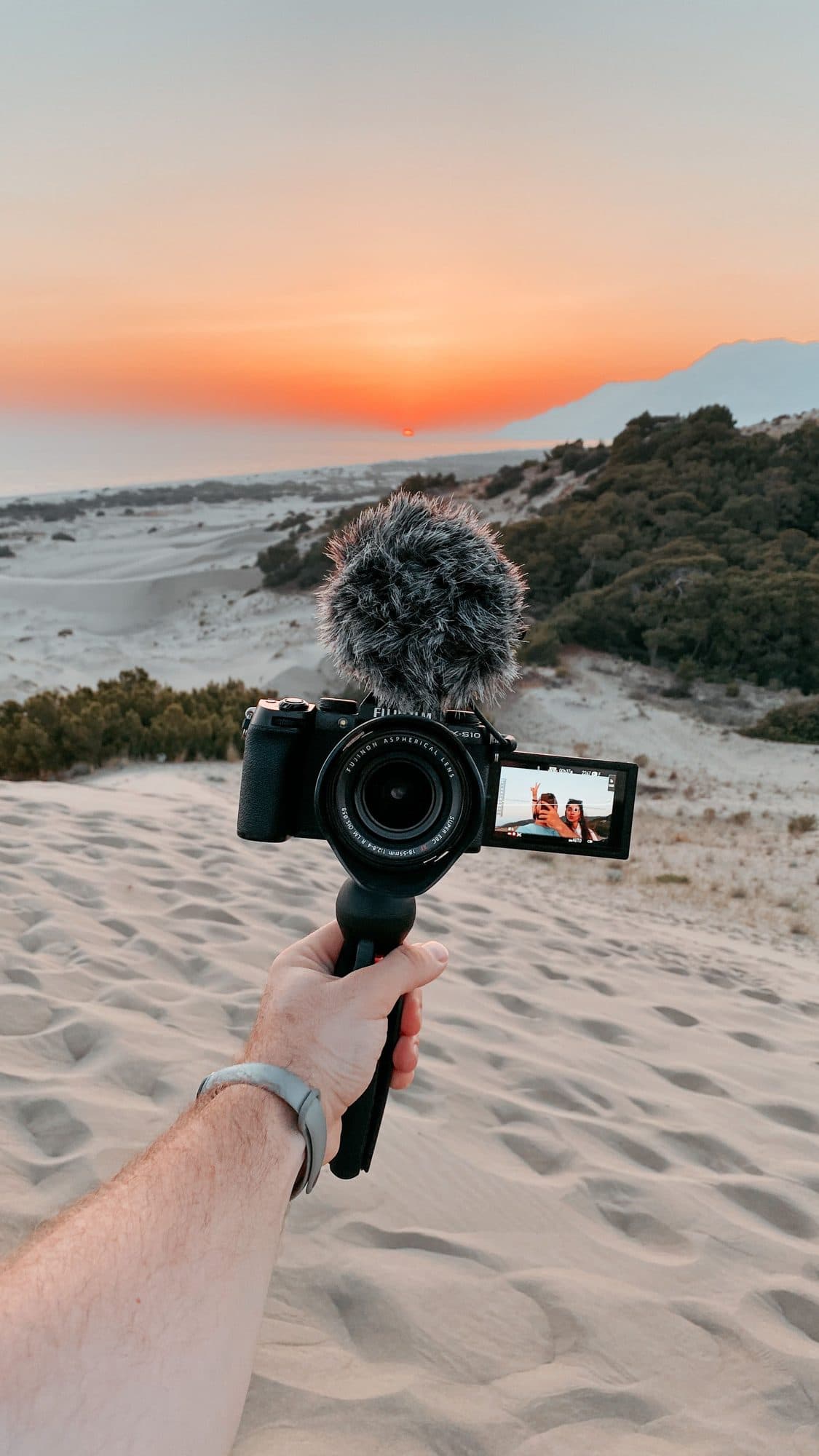 Creator filming on a handheld camera on a beach at sunset